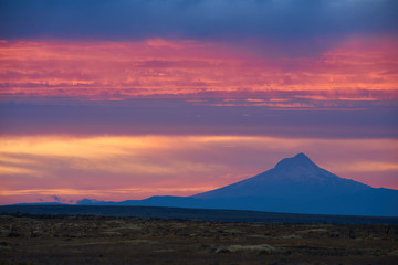 Colorful surrealistic Landscape with Mount Hood silhouette and dramatic clouds in the sky at sunset sunlight. View from viewpoint in Eastern Oregon USA Pacific Northwest.