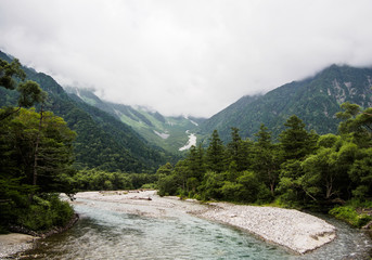 The view of the stream flows down through the forest on the mountain with cloud background at Kamikochi Japan