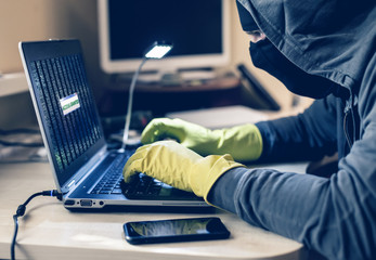 Computer Criminal in balaclava and gloves doing protection hack