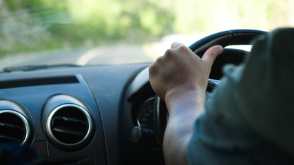 Close up of male hand on the steering wheel driving a car in the long road along mountains