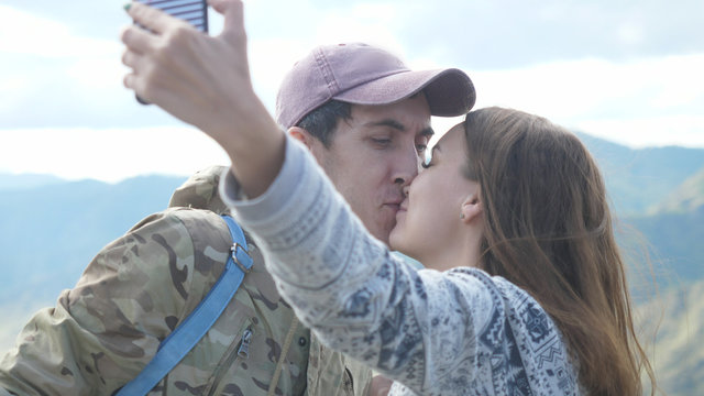 Happy young couple on the mountain top taking selfie photo while kissing