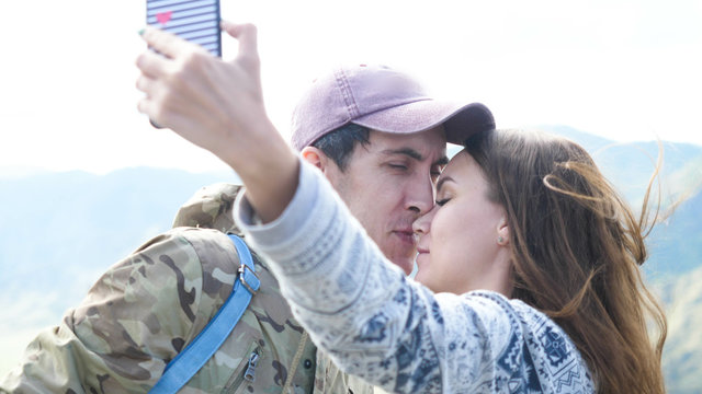Happy beautiful couple on the mountain top taking selfie photo while kissing