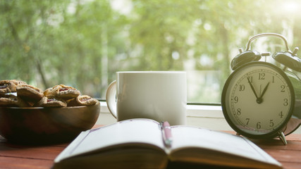The opened book and standing next to the clock with the biscuit and cup of tea the concept of...
