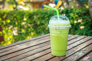 Iced green tea with green straw in a plastic glass on the natural garden background.