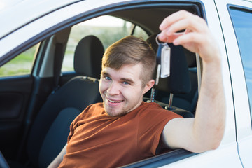Happy young smiling man sitting inside new car with keys.
