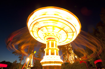 Colorful chain swing carousel in motion at amusement park at night.