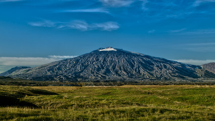 Panoramic view of black volcano Snæfellsjökull with blue sky above and green dry grass below . West Iceland, Europe.
