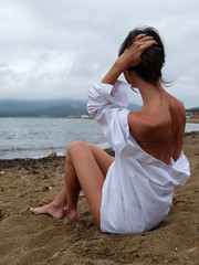 The girl sits on the shore of the Japanese Sea in a white shirt.
