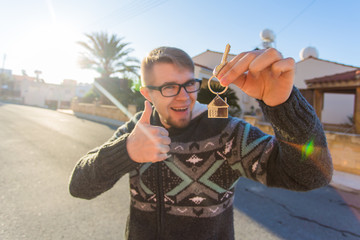 Portrait of a young funny man holding new house key and gesturing thumbs up - new home or apartment concept