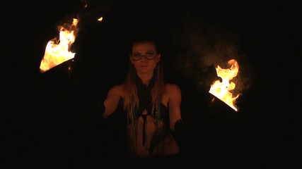 Portrait of a young mystic woman in the dark forest spining bowl of fire close to face in front and back of head. Woman with fire over dark night background.