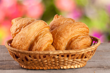two croissant in a wicker basket on a wooden board with a blurry garden background