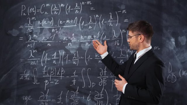 Young caucasian man teacher lecturer in formal suit and tie explaining decision of hard math equation. He invite You to study in university, smile and looks smart and clever.
