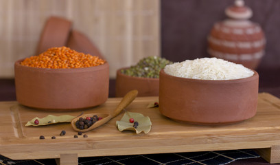 White rice, red lentils and green peas mache on wooden tray. Bay leaves and black peppercorns in...