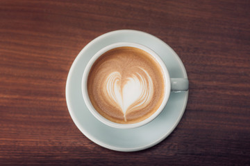 Top view of hot cappuccino with latte art in pastel blue cup on dark brown wood table near window in morning,vintage filtered,