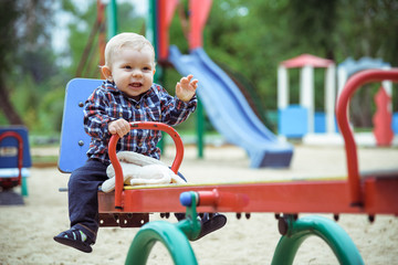 Happy little baby boy playing on the playground in the summer or autumn day