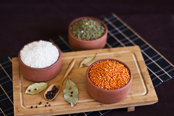 White rice, red lentils and green peas mache on wooden tray. Bay leaves and black peppercorns in wood spoon.