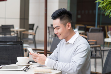 Young Asian happy man text messaging on social media application by smartphone during coffee time in cafe, casual lifestyle in summer holiday or vacation time concepts