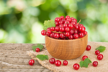 Red currant berries in wooden bowl on wooden table with blurry garden background