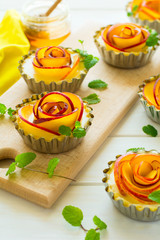 Tartlets with plum roses decorated mint leaves on white wooden background. Selective focus