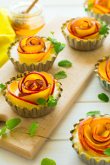 Tartlets with plum roses decorated mint leaves on white wooden background. Selective focus