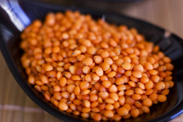 Red lentils in black glass plate. On wooden table. Macro