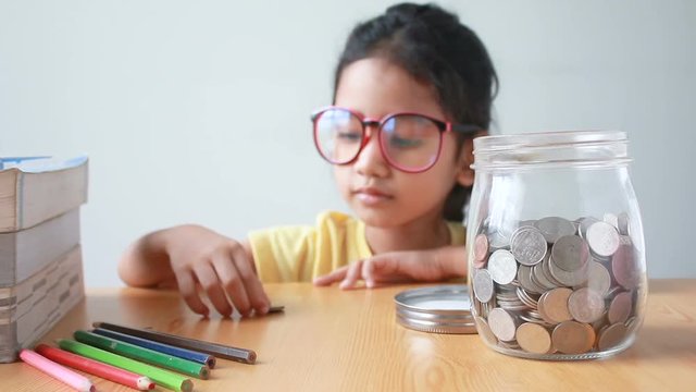 Asian little girl putting the coin into a  clear glass jar on table metaphor saving money concept with sound select focus on jar