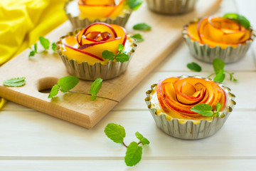Tartlets with plum roses decorated mint leaves on white wooden background. Selective focus