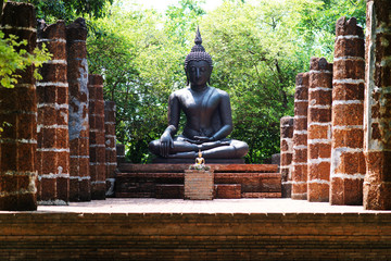 A big black buddha surrounding by orange bricks column in green garden