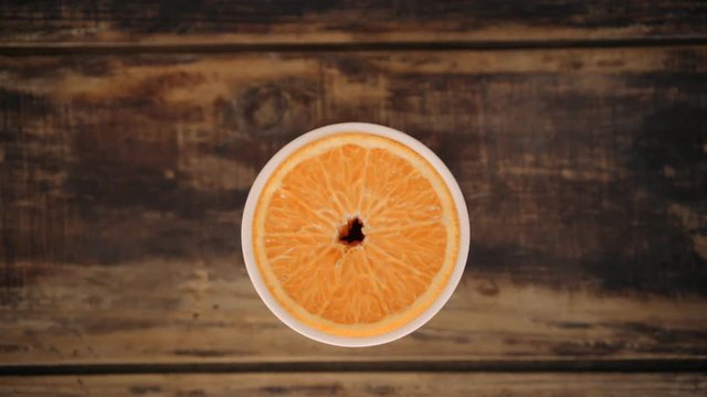 Close up of hand putting ceramic cup or glass on top of aged wooden hipster table or tray, with sliced orange fruit in middle and then sticking a blue cute straw inside to enjoy drink or juice