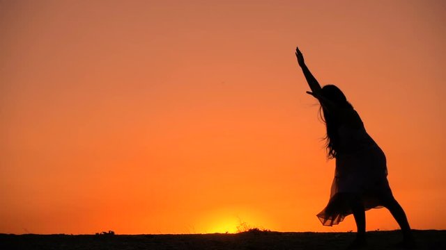 Silhouette of young girl standing somersault against sunset