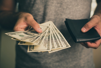 A man holds dollars and black wallet in his hands
