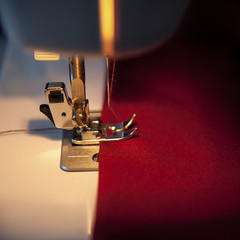Sewing hobby background. Sewing machine with red fabric. Close up process with copy space. Dramatic...