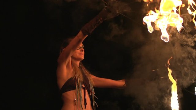 Young girl with beautiful eyes dances with burning torches made in shape of fans at fire show. spinning overhead