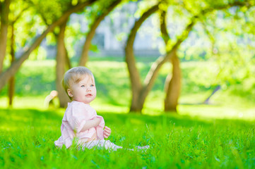 Cute baby girl sitting on green summer grass