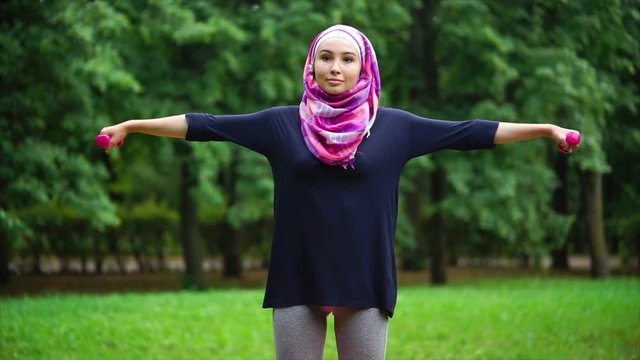 Young Muslim woman having outdoor workout. She keeping fit with regular trainings including exercises with dumbbells