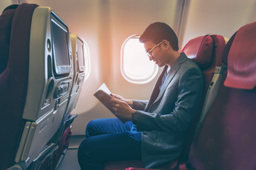 Fototapeta premium Young asian business man smiling and reading a book in airplane