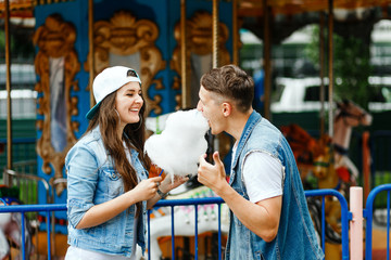 Young fun couple biting into a cotton candy floss sweet at the same time while visiting an...