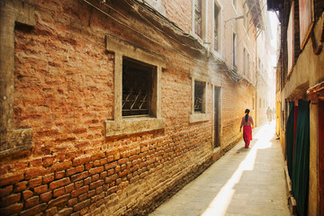 Fototapeta na wymiar Narrow street in Kathmandu old town, Nepal, Asia. Woman walks down the street in sunlight. Toned.