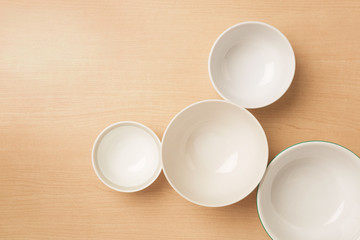 Four empty bowls on light wood background, Flat top view