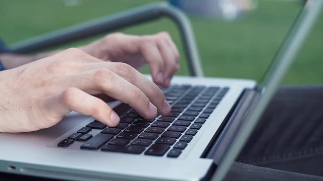 Male hands typing on laptop. Outdoors. City park. Summer day. Freelancer working outdoors.