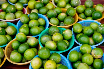 Stack of Green local lemons in plastic baskets on wood table for sell in the market.