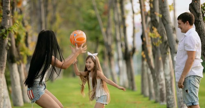 Young parents playing ball with little girl in the park. slow motion