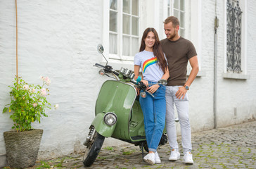 Image of young happy loving couple holding map outdoors near scooter. Looking aside.