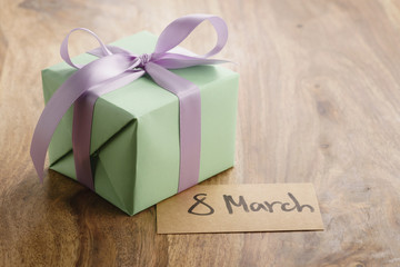 green paper gift box with purple ribbon bow and 8 march greeting card on old wood table