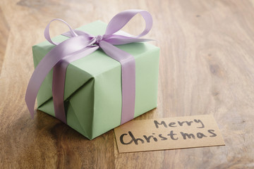 green paper gift box with purple ribbon bow and merry christmas greeting card on old wood table