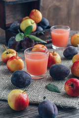 Fresh plum juice. The juice in the glass is surrounded by plums and apples on a wooden table. Still Life with Plums