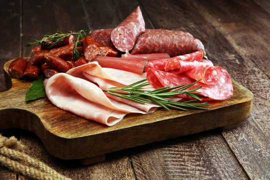 Marble cutting board with prosciutto, bacon, salami and sausages on wooden background. Meat platter