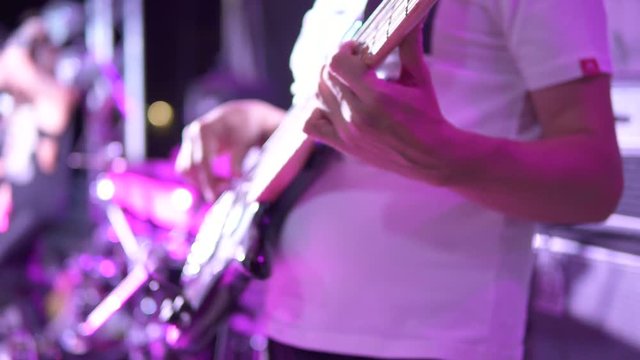 Closeup view of male hands playing bass guitar in blue neon light. Musician playing bass guitar live during the show concert in a night club
