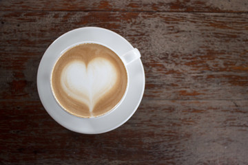 Hot coffee on table with heart shape on top of white cup from top view. Copy space.