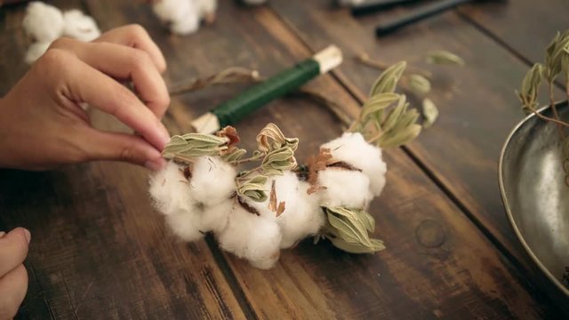 Hand held shot of beautiful romantic and tender arrangement of cotton flower blossoms with green leaves and flexible branches in wedding bride gown crown to create image.
